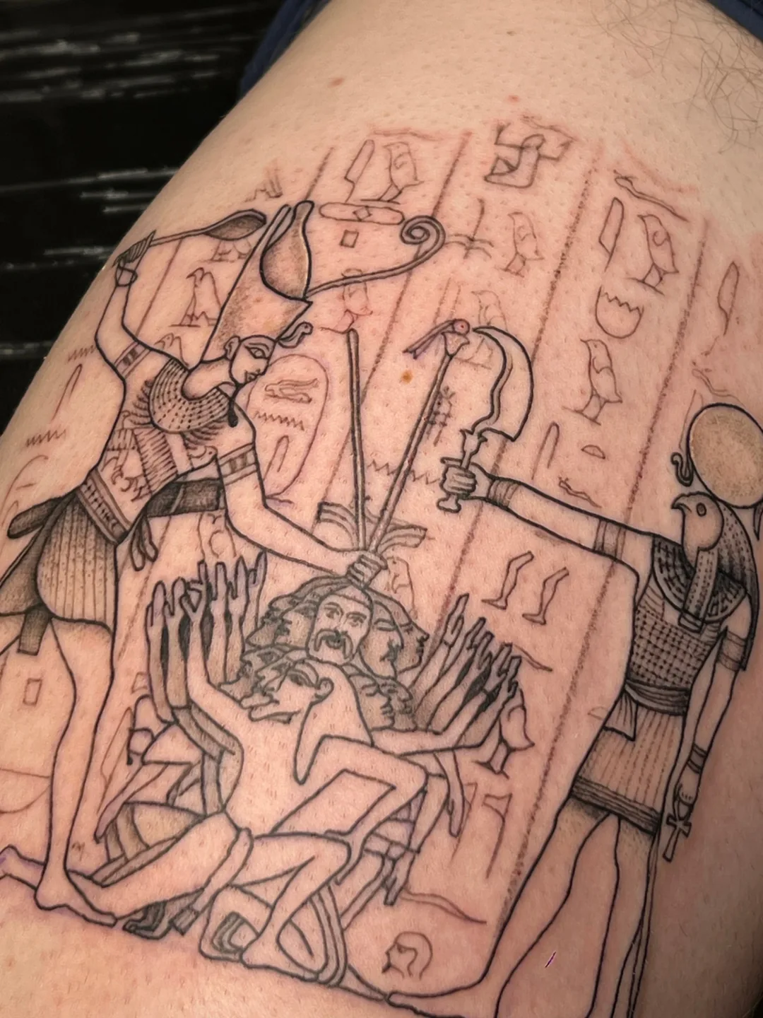 Fine-line tattoo of an ancient Egyptian relief scene with hieroglyphs on a thigh