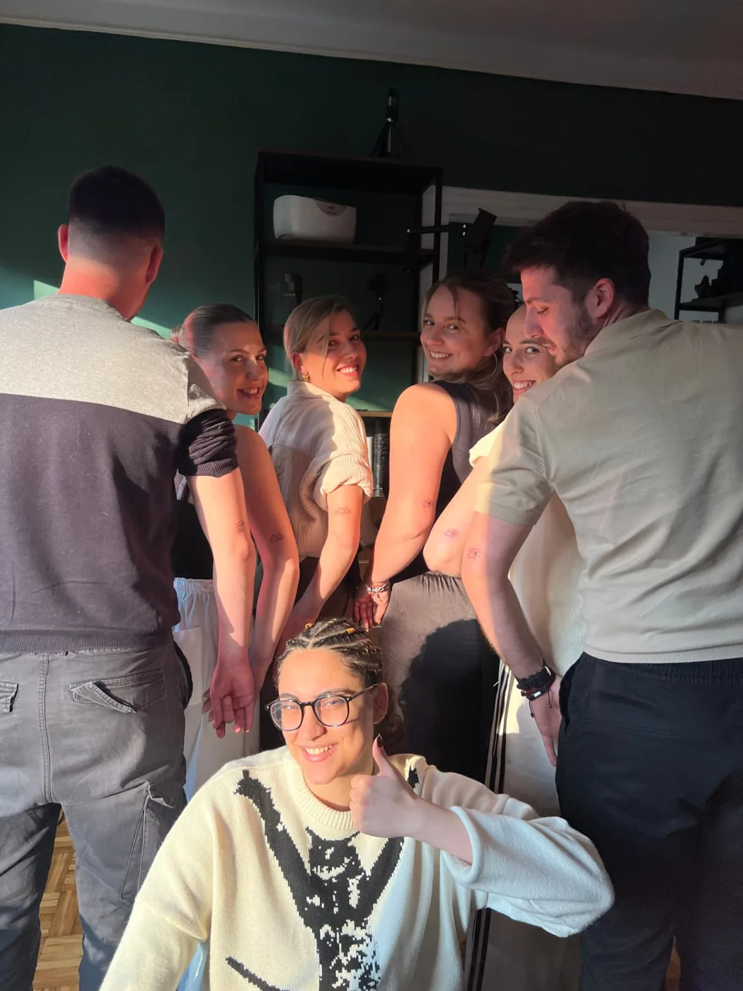 A group of guests together in the studio showing small matching fine-line tattoos on their arms